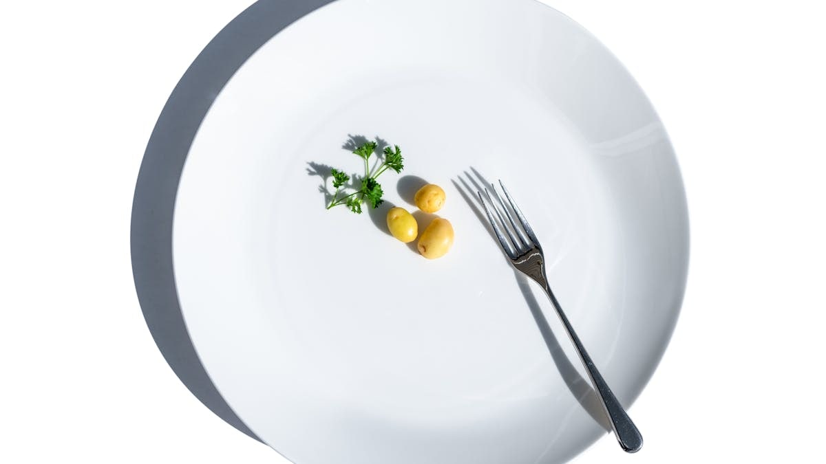 Minimalist still life of potatoes and parsley on a white plate with fork, symbolizing dieting.